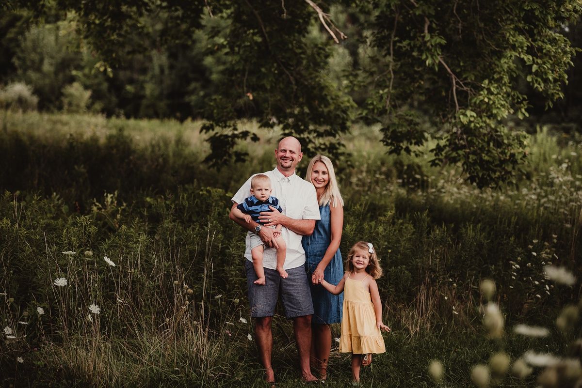 Family portrait of three people standing together in a wild meadow at sunset.