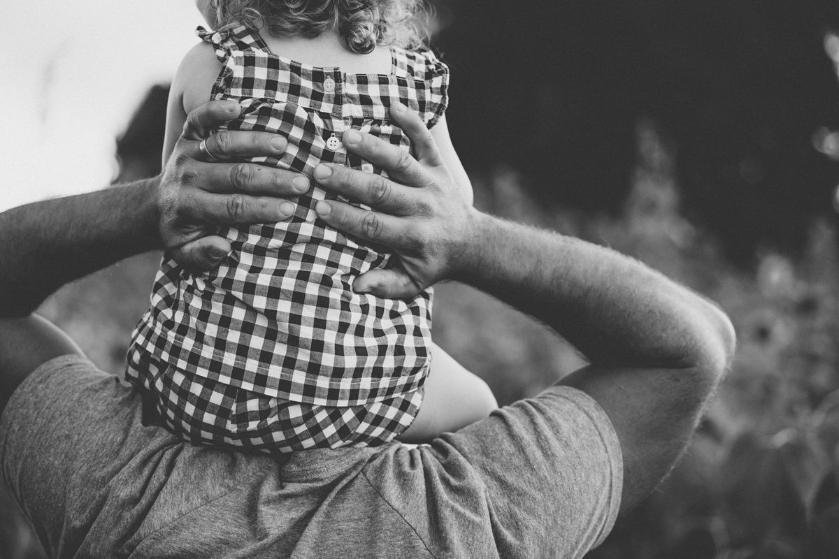 Black and white close-up of shoulders carrying a child in gingham pattern clothing.
