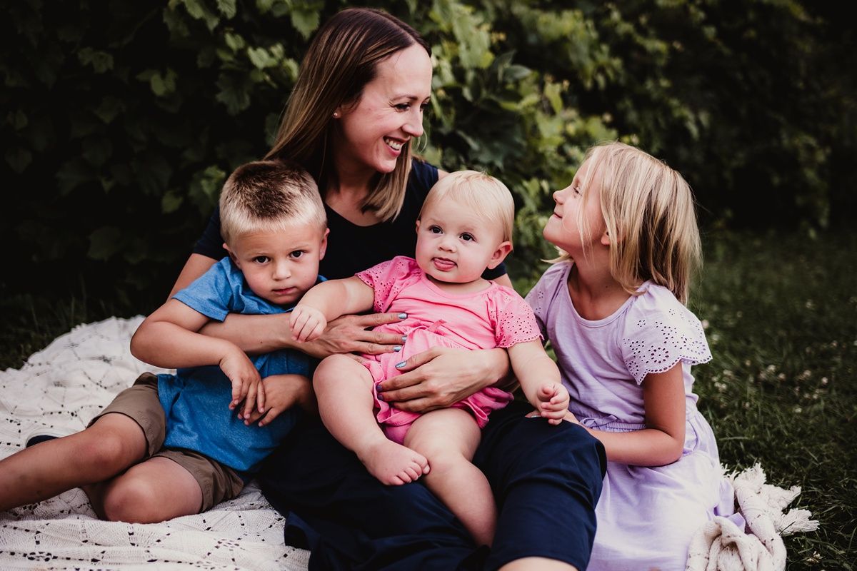 Candid family portrait on a blanket outdoors with natural lighting and greenery background.