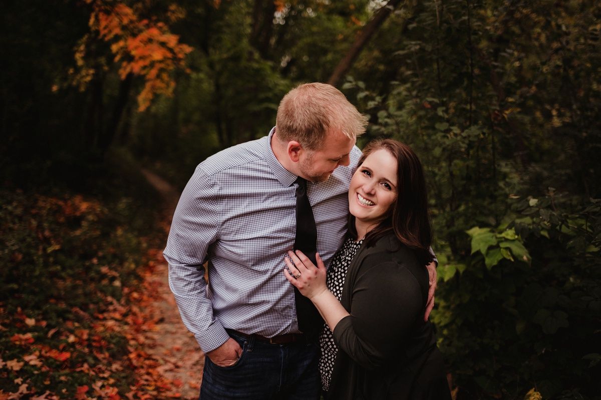 Romantic autumn photo shoot of couple laughing together in wooded area with fall foliage.