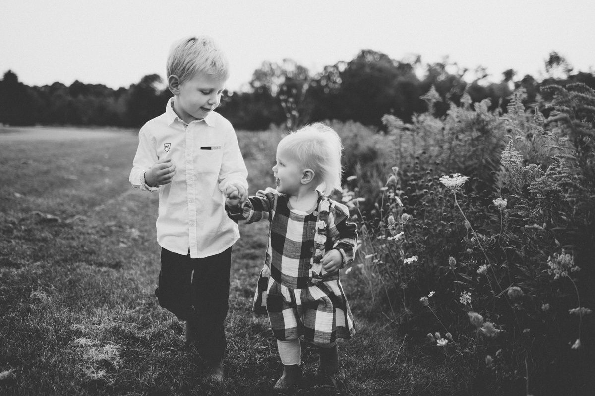 Children examine wildflowers in a meadow in black and white photography.