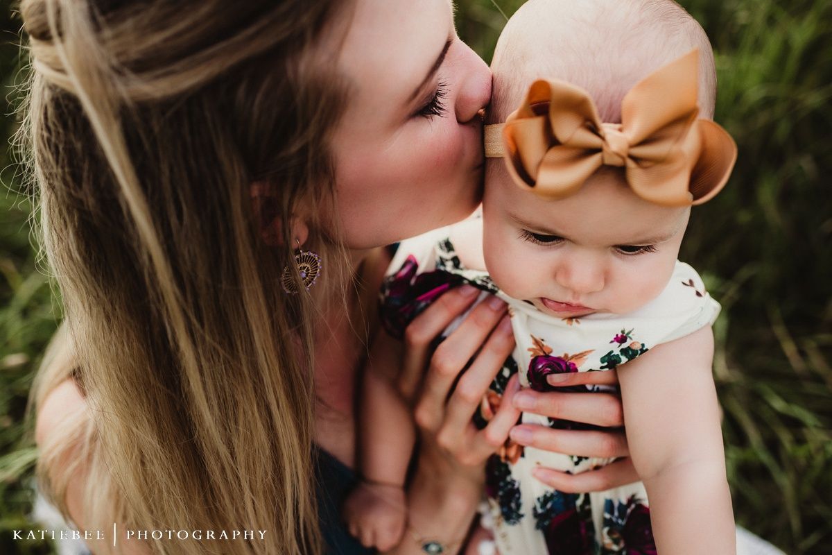 An intimate mother-child moment captured outdoors with a baby wearing a brown bow headband.