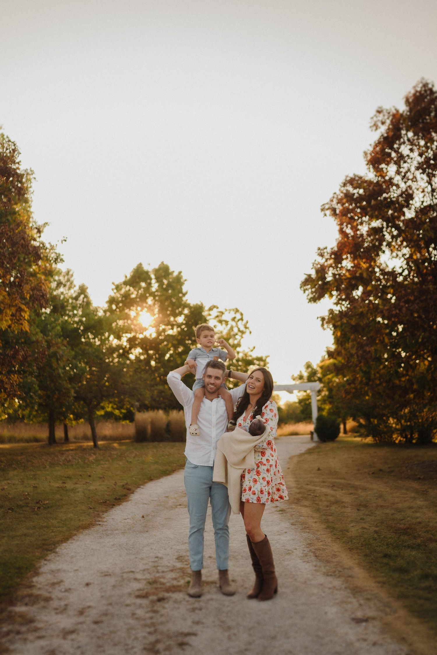 Family sharing joyful moment on tree-lined path during golden hour.
