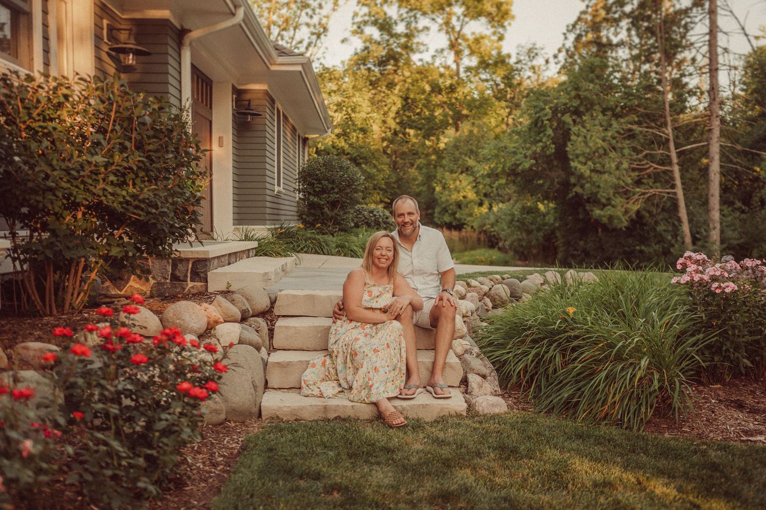 Couple sitting on stone steps surrounded by landscaping and flowers at sunset.