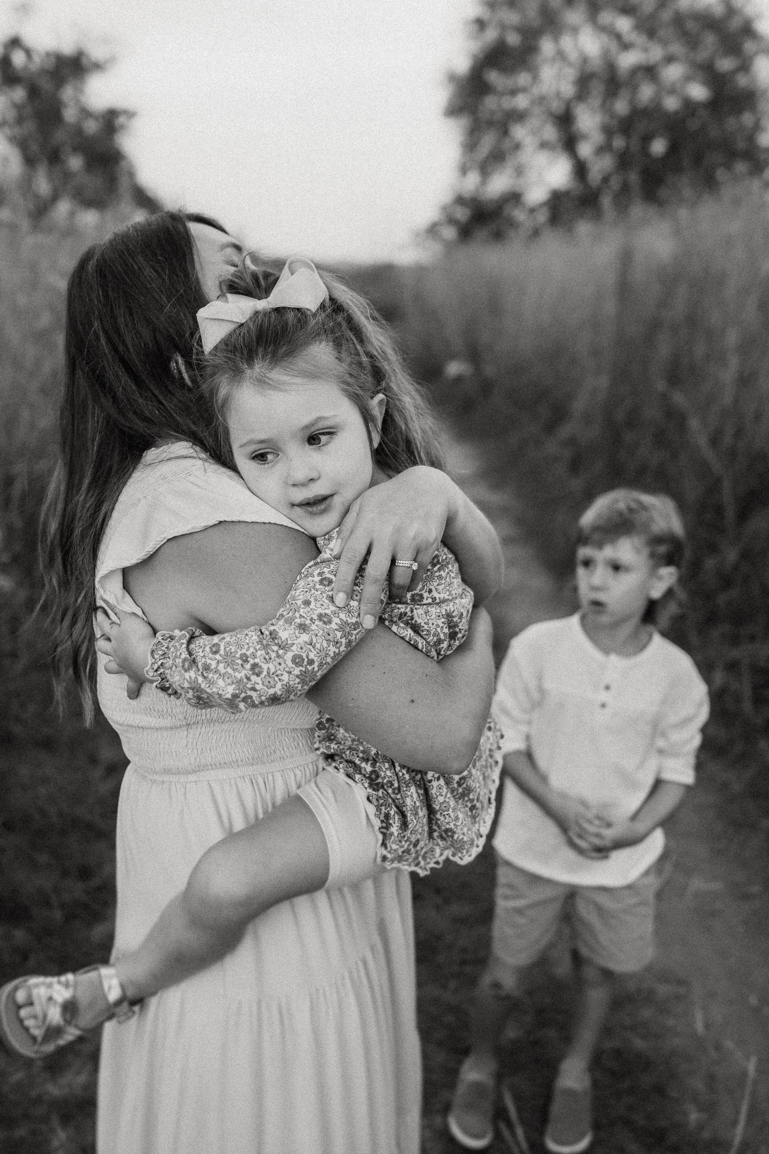 Black and white candid family photo on outdoor trail with tall grass background.
