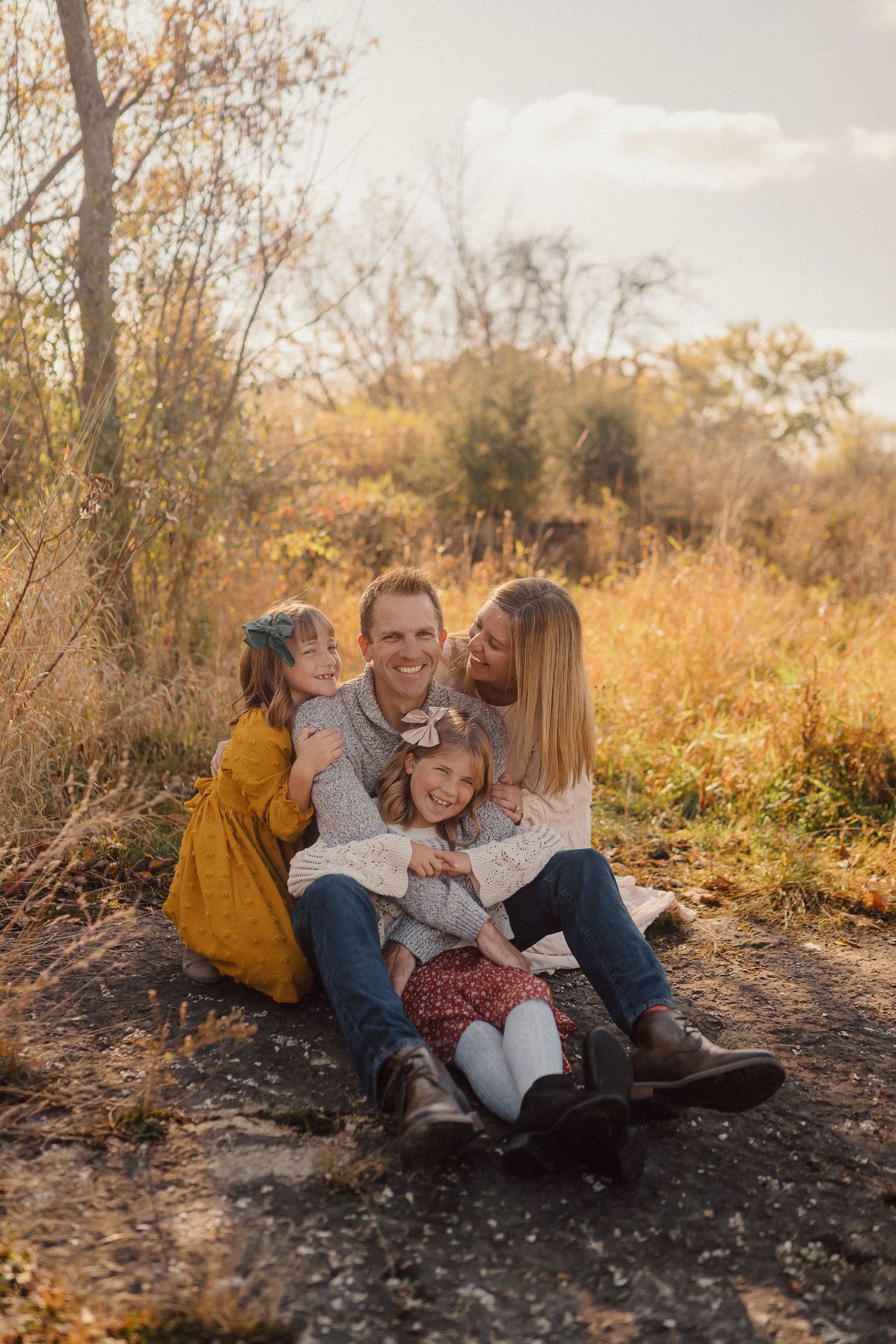 A family embracing and laughing together on ground during fall sunset photoshoot.