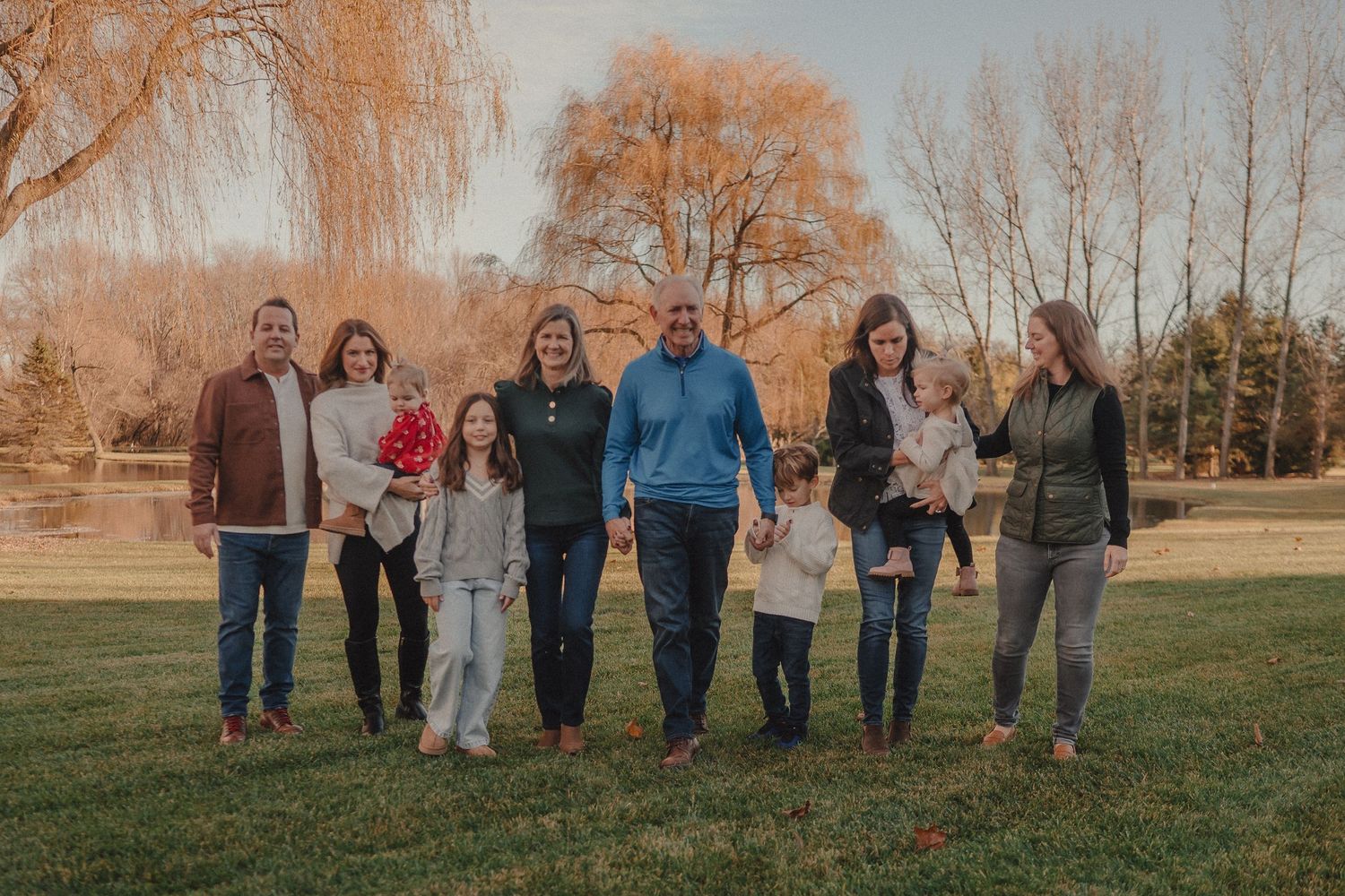 Wide panoramic shot of a group standing together on grass with bare trees in the background.