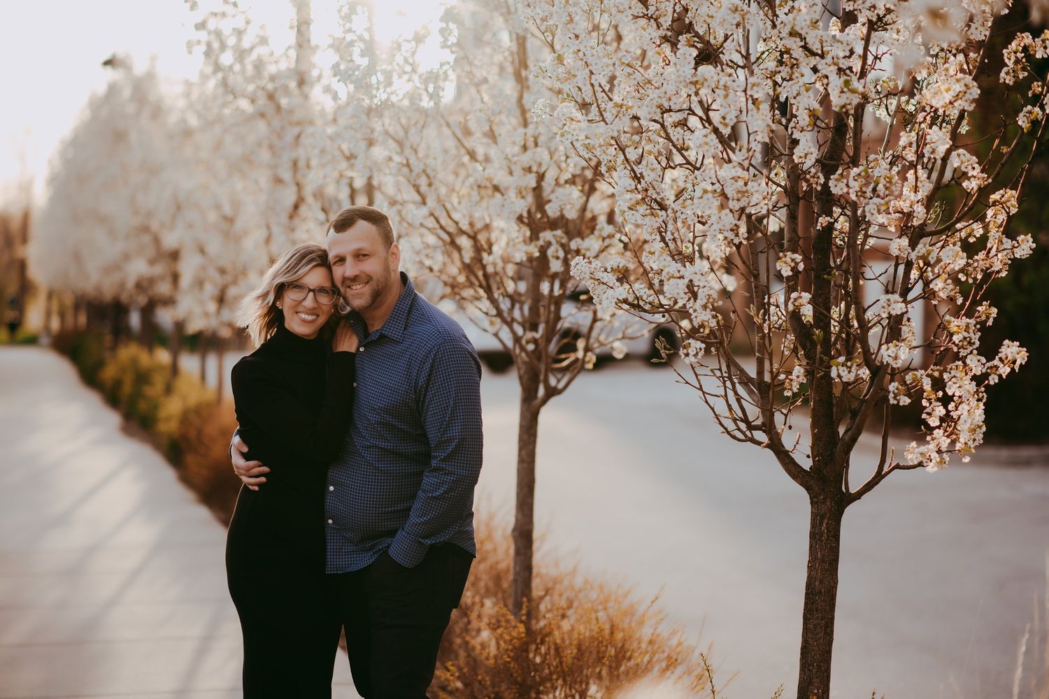 Happy couple embracing outdoors with blooming cherry trees lining the street.