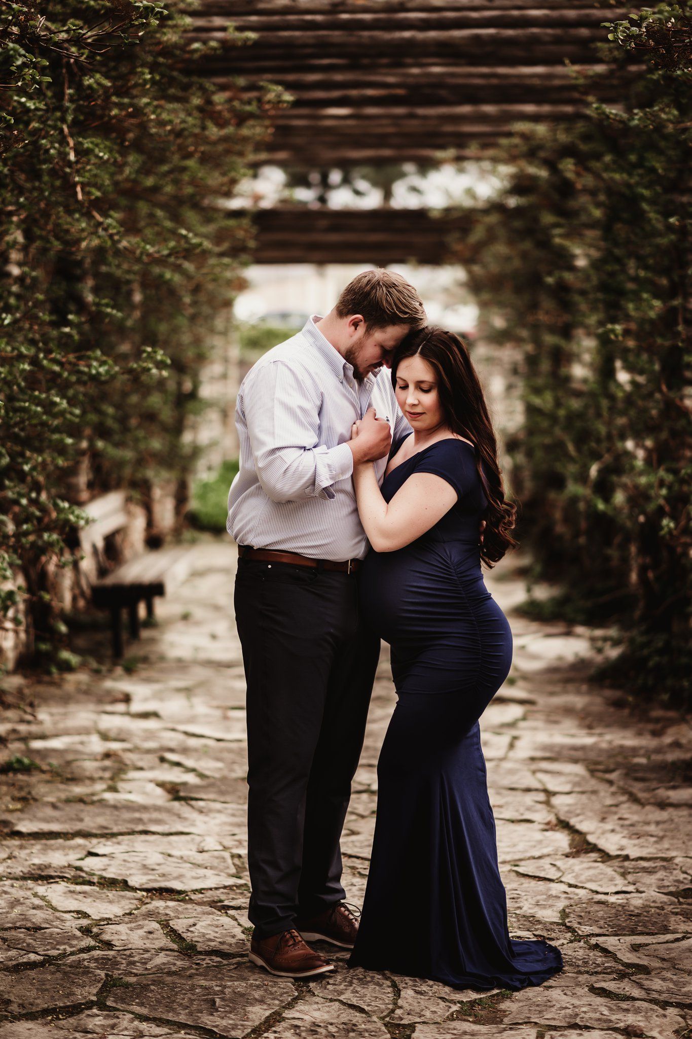 Romantic maternity photo on stone path under wooden pergola.