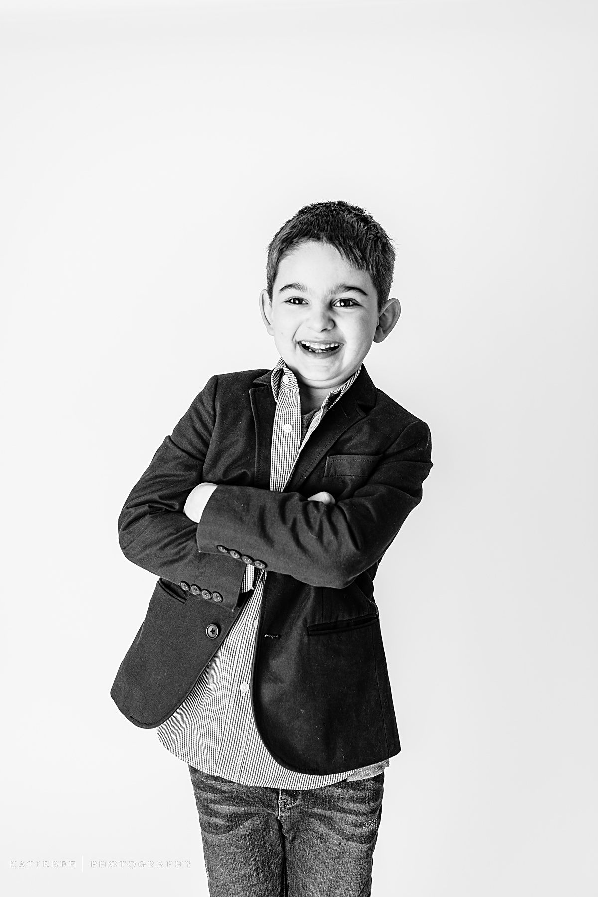 Monochrome portrait of smiling child in dark blazer with crossed arms against white background.