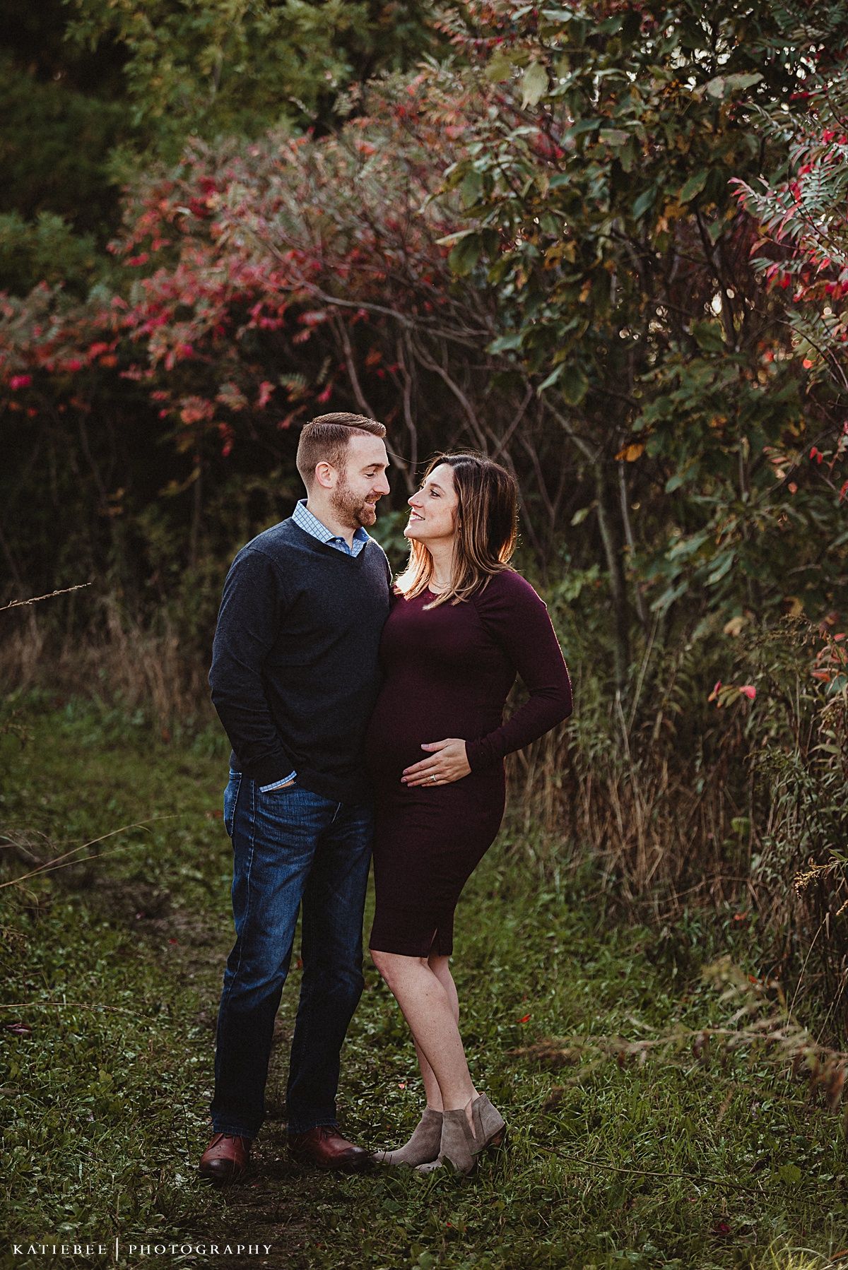 A couple shares an intimate moment outdoors surrounded by fall foliage.
