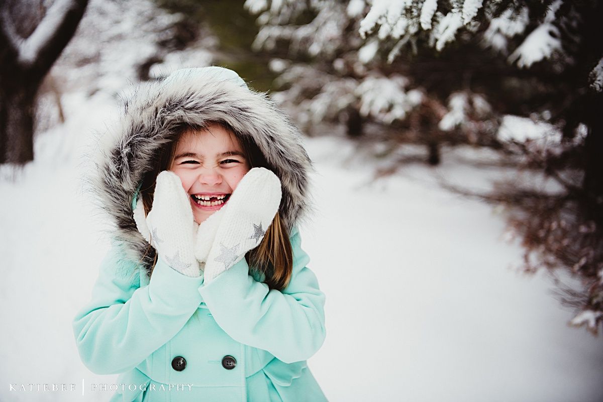 Person in mint coat and fur hood laughing in winter snow scene.