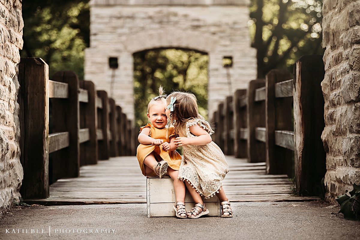 Sweet moment shared between two children sitting on a wooden bridge with stone pillars.