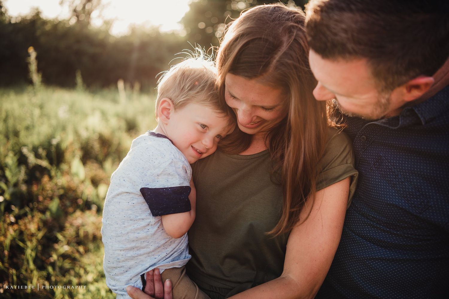 A tender family moment at golden hour in a grassy field outdoors.