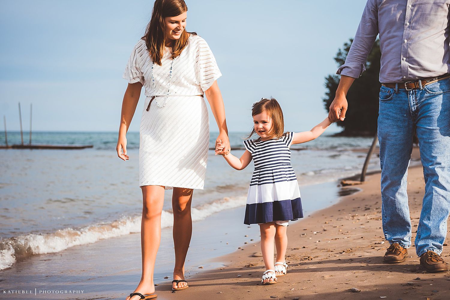 A family walks hand in hand along a sunny beach shoreline.
