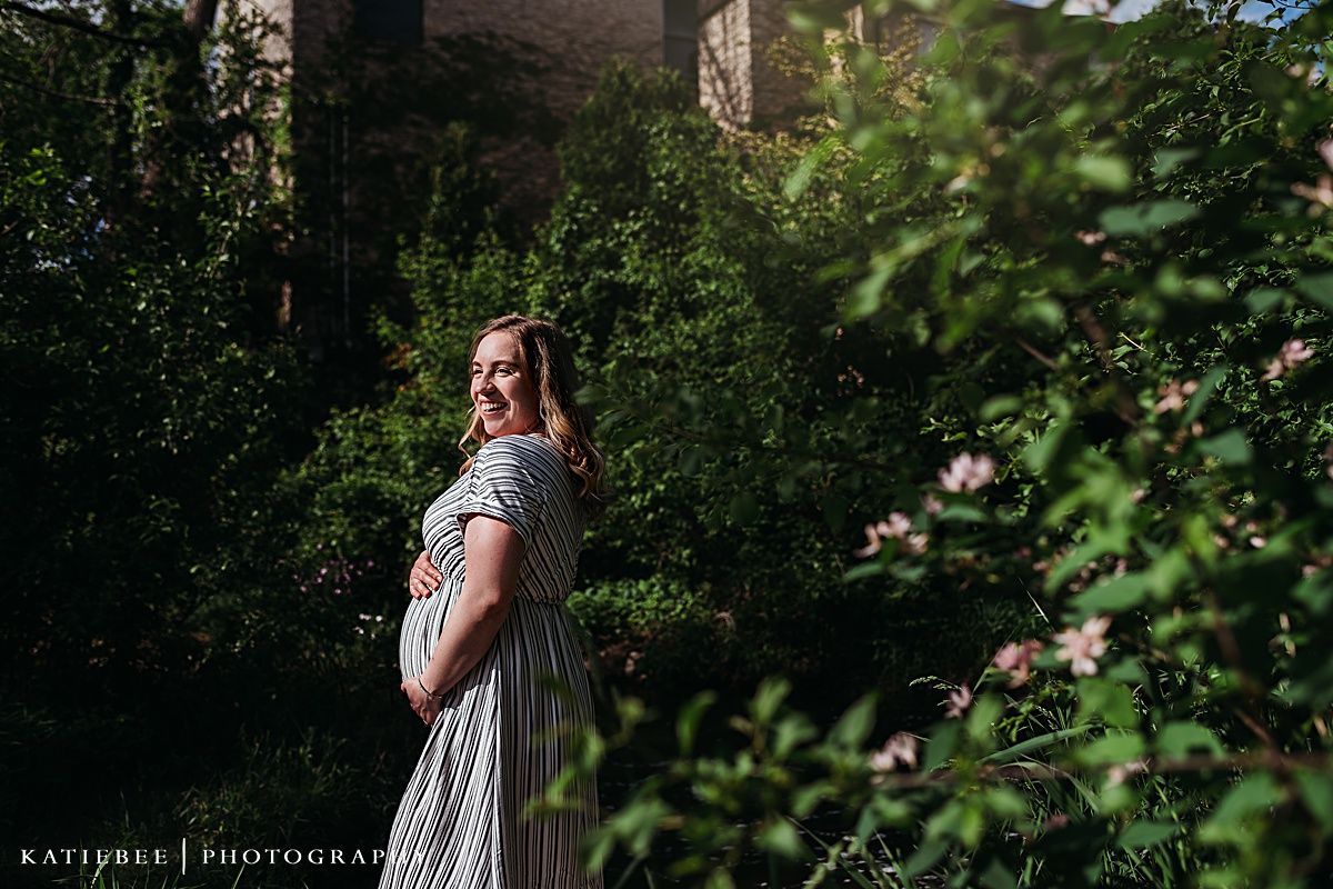 A maternity photo in a garden setting with a striped dress capturing an expectant moment in natural lighting.