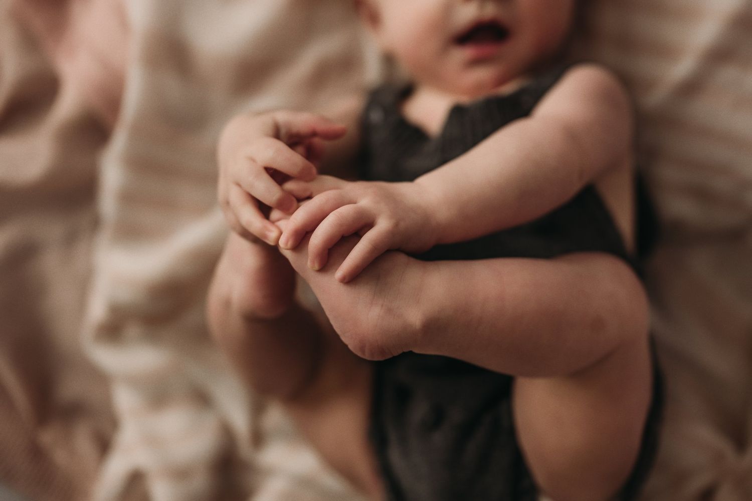 Close up photo of baby's hands in soft lighting on neutral backdrop.