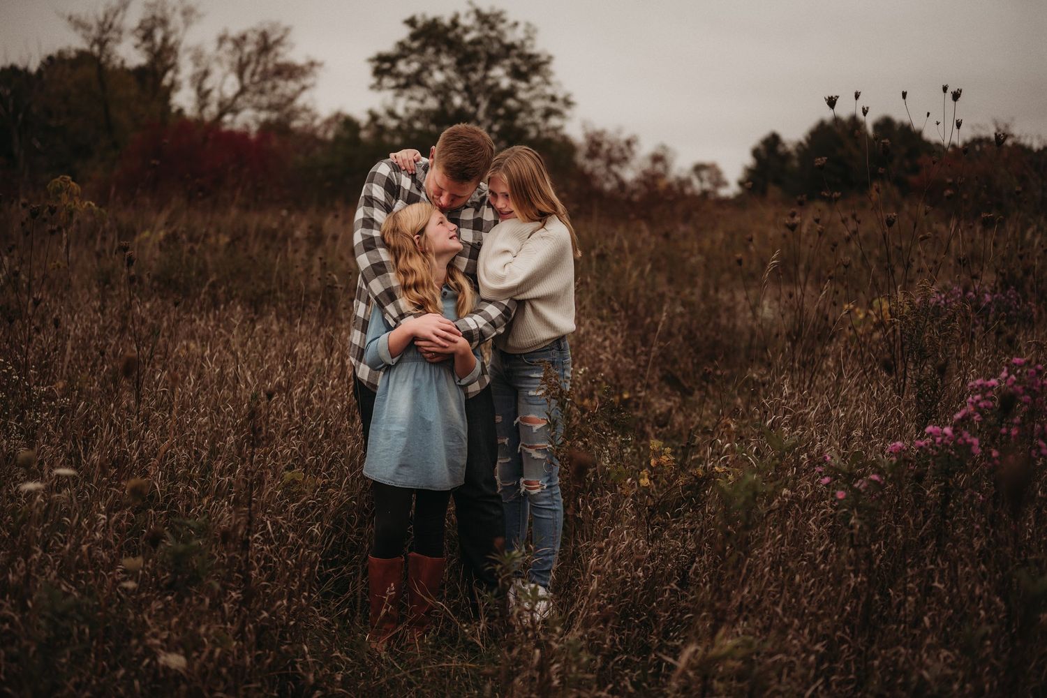 Intimate family moment captured in moody tones among tall grasses at sunset.