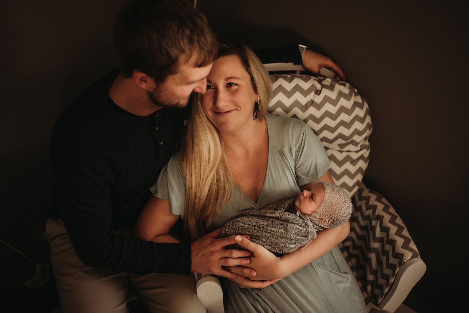 Tender family moment captured in cozy nursery setting with chevron chair.