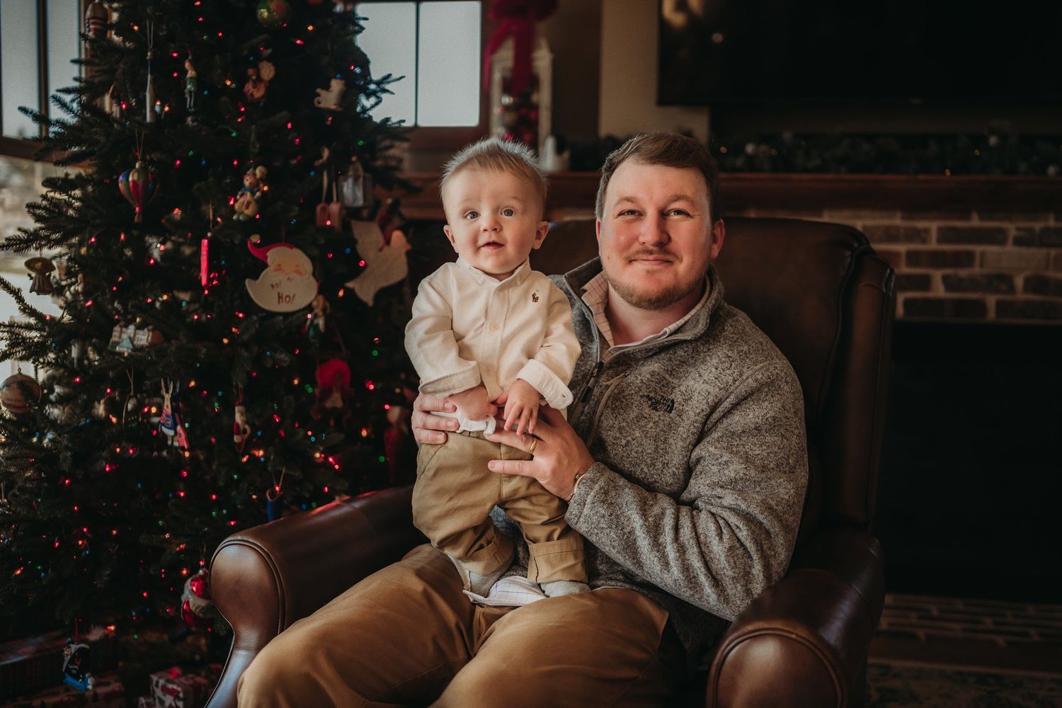 Christmas portrait by decorated tree with twinkling lights and exposed brick wall.