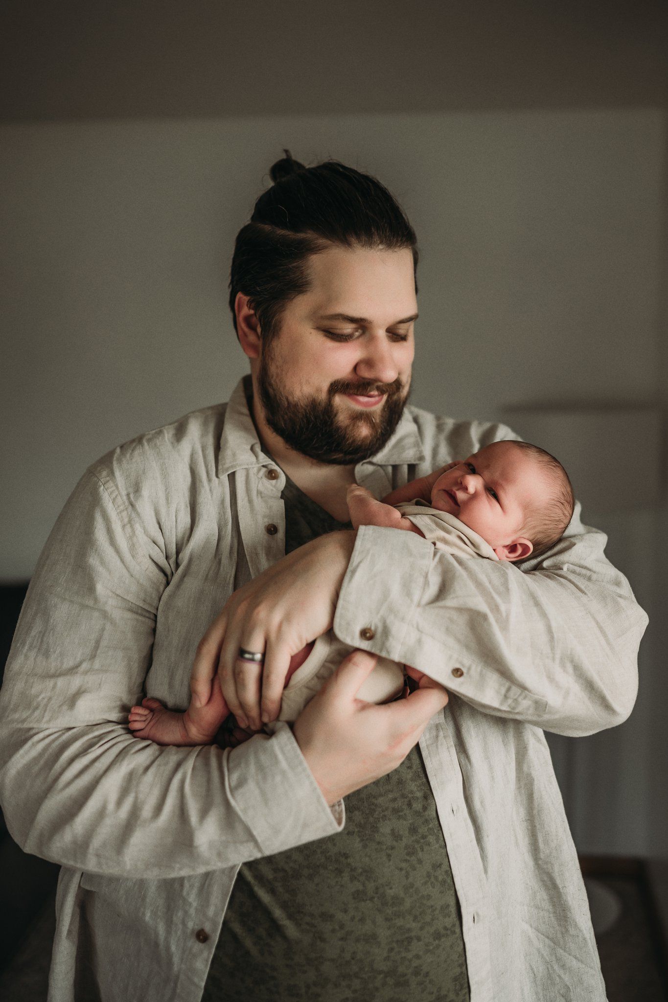 Someone wearing a light colored button-up shirt gently holds a sleeping newborn baby.