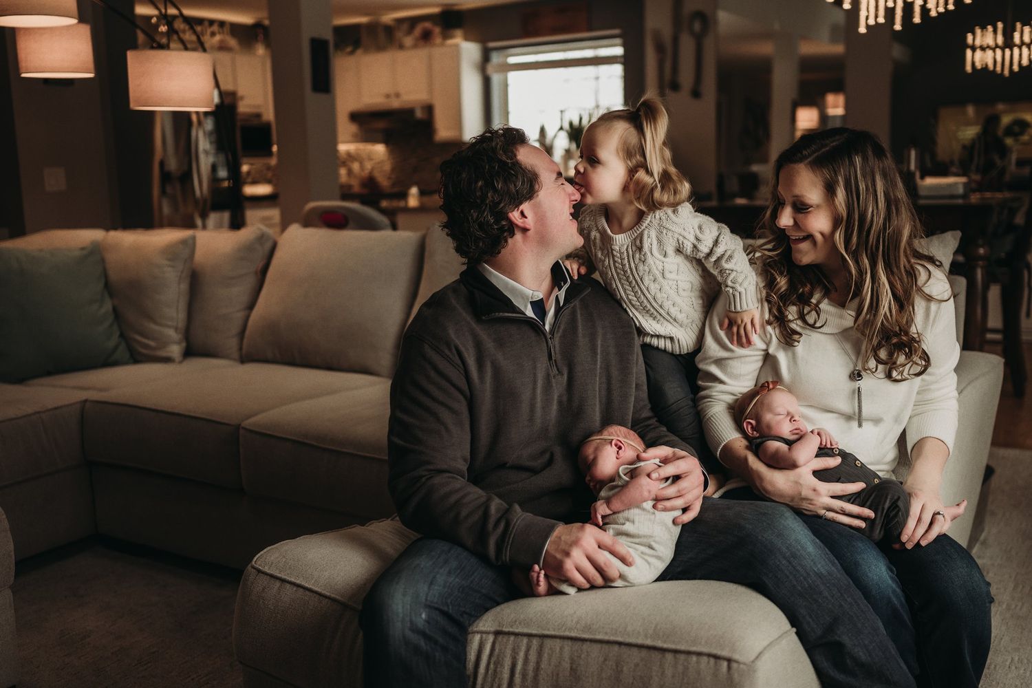 A family relaxes together on a couch in their living room with infants.