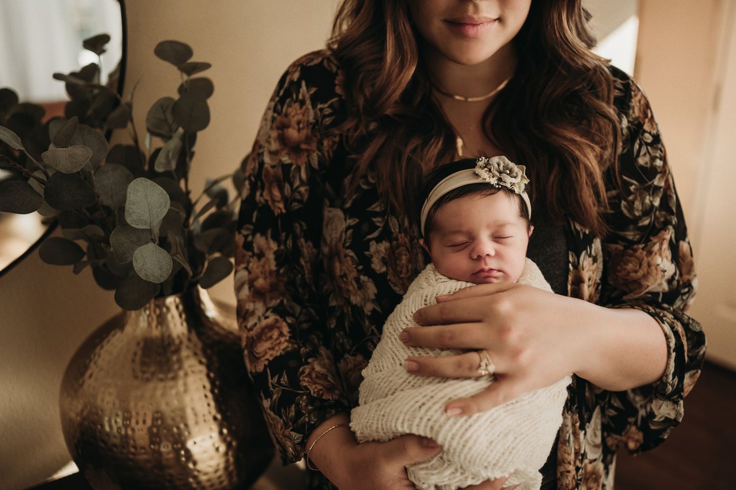Cozy indoor scene with floral pattern dress and soft white swaddled baby near decorative vase.