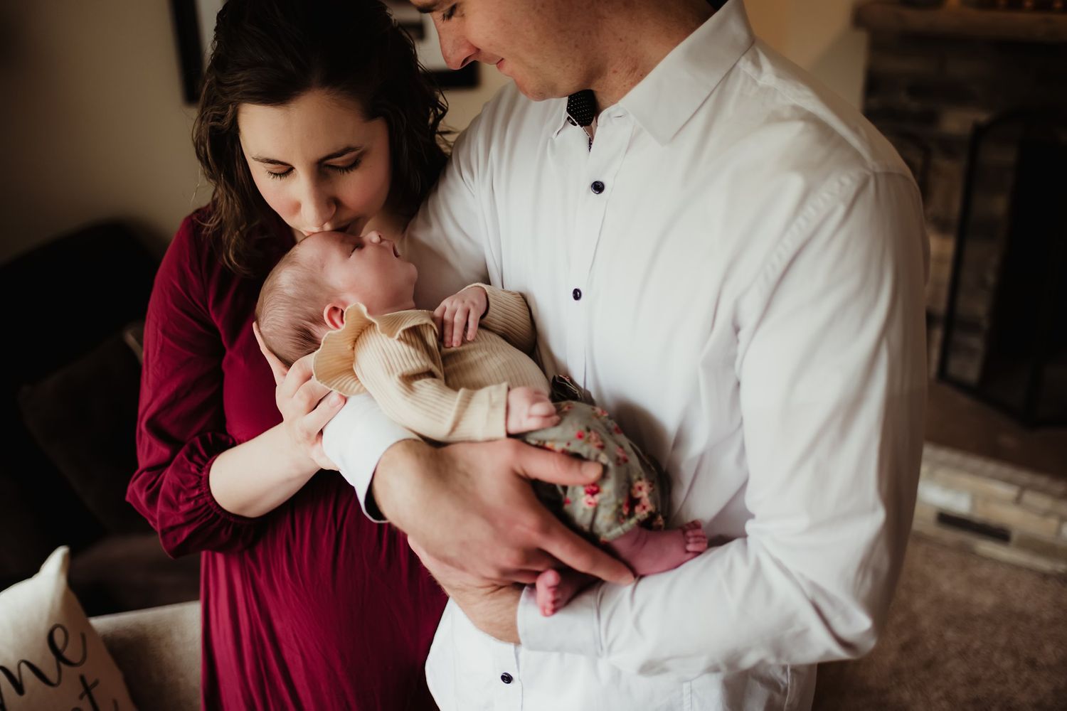Parents in white shirt and burgundy dress lovingly gazing at their newborn baby.