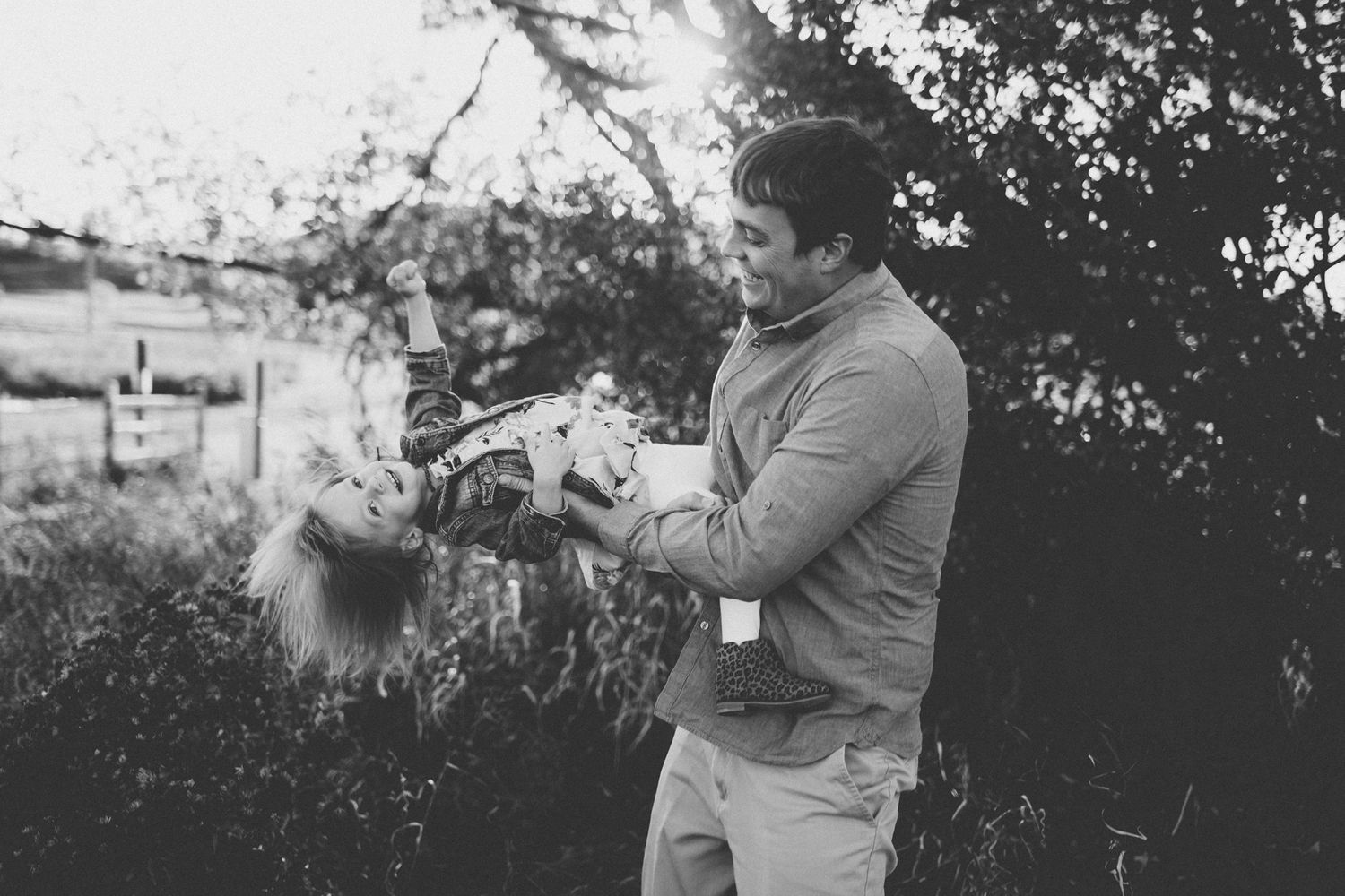 Black and white photo of a person holding and playing with someone in an outdoor setting.
