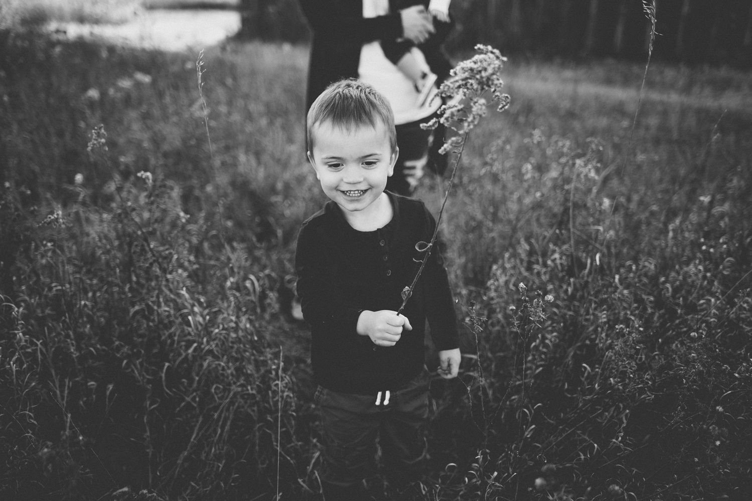 Young child playing in tall grass during a black and white photo session.