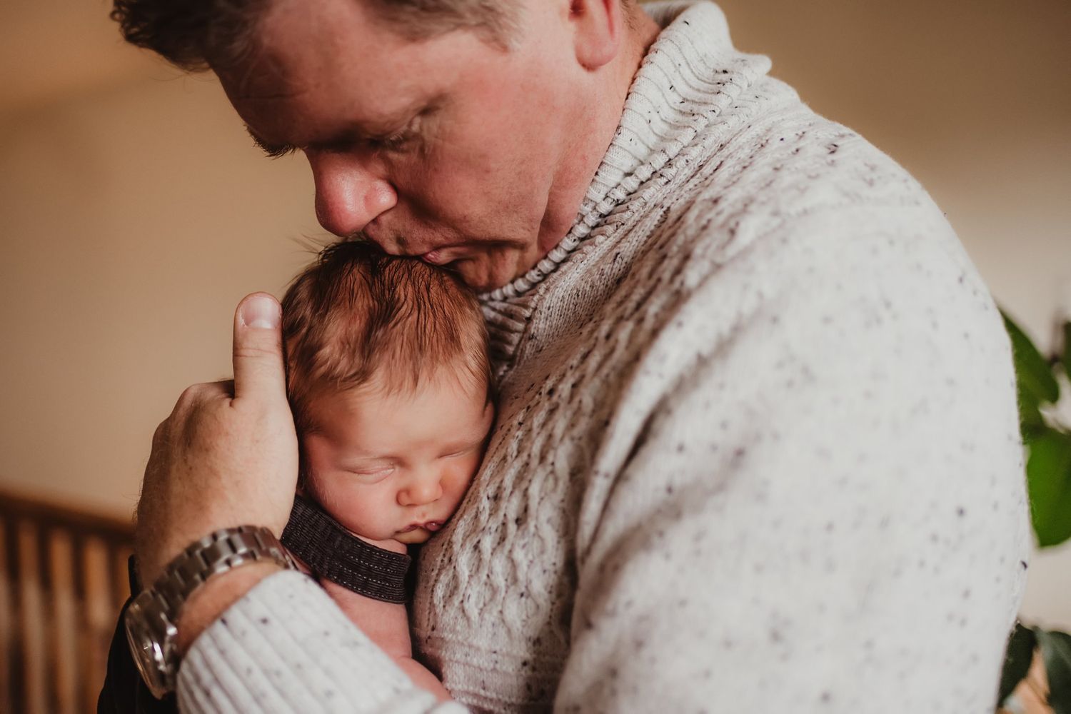 Gentle moment showing adult in cream sweater cradling sleeping infant.