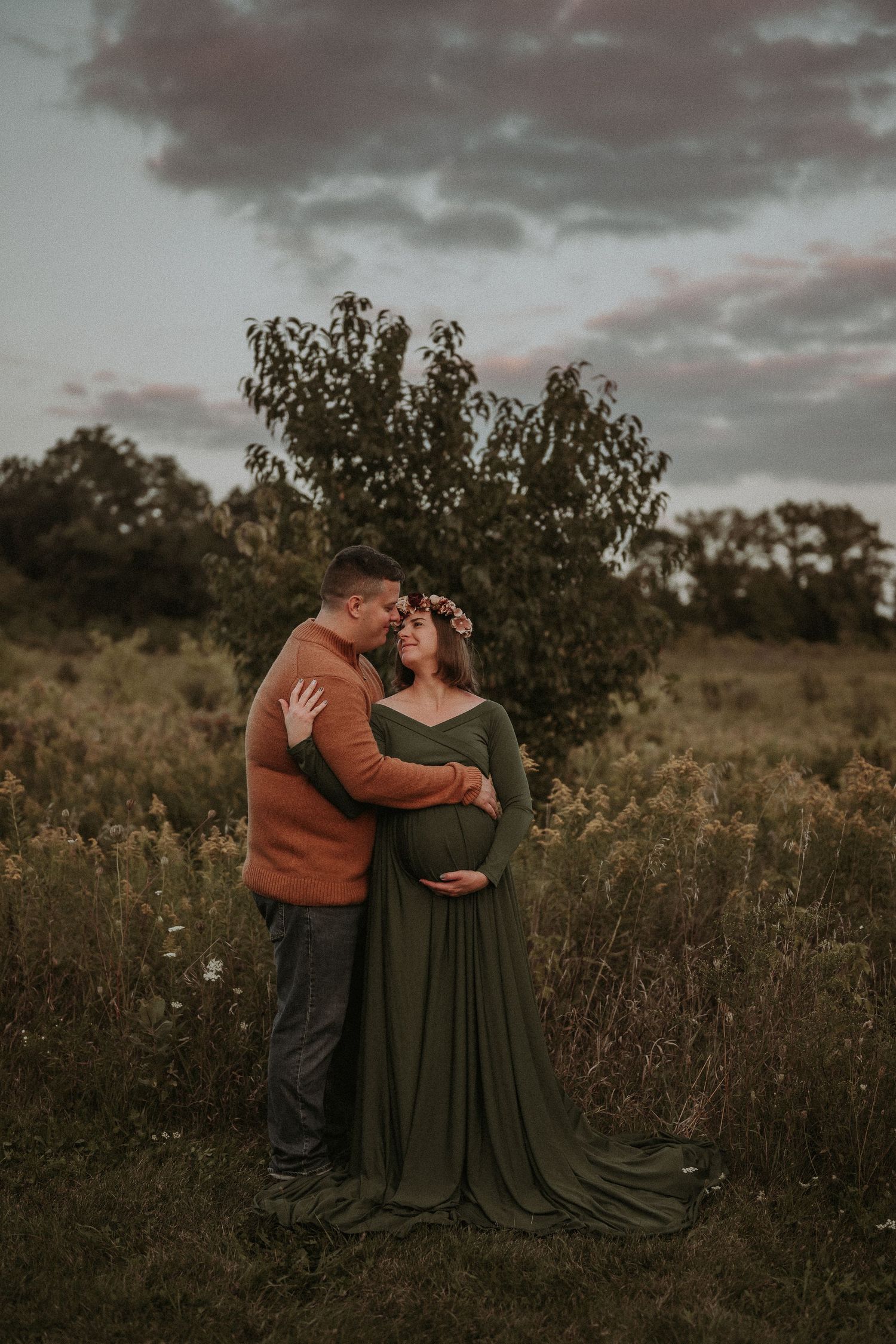 Intimate maternity portrait of couple embracing in field at dusk.