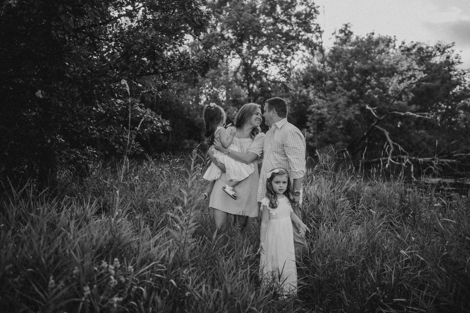 A family shares a tender moment together in tall grass at sunset in black and white.