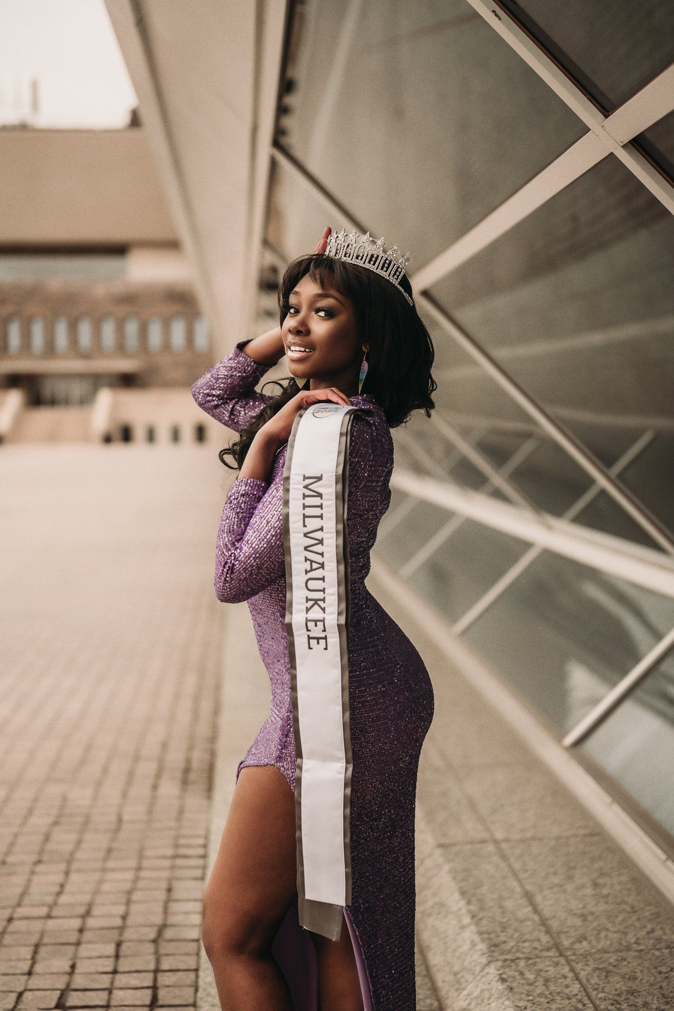 Beauty queen in purple evening gown with Milwaukee sash poses elegantly.