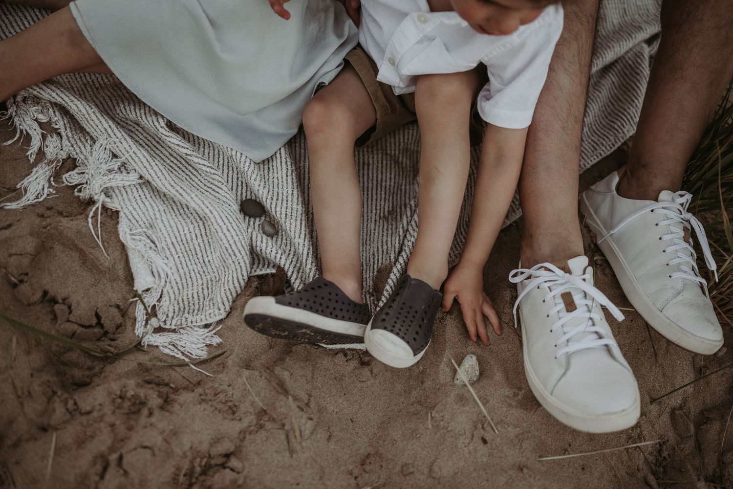 Close-up shot of family feet in sneakers sitting together on sandy ground.