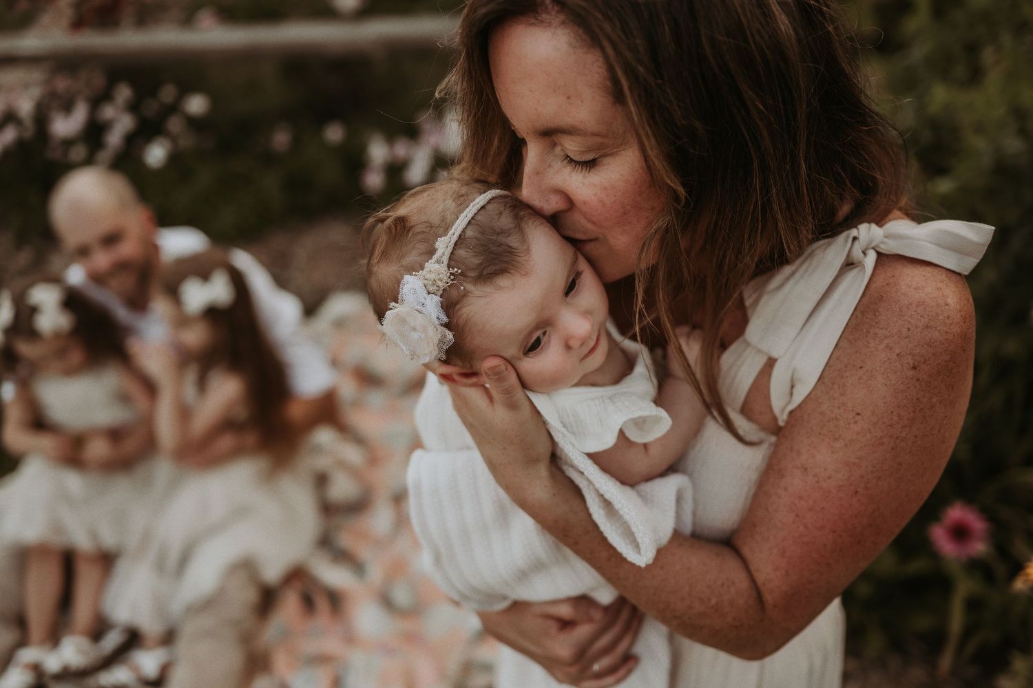 A tender moment captured between parent and baby dressed in white outdoors.