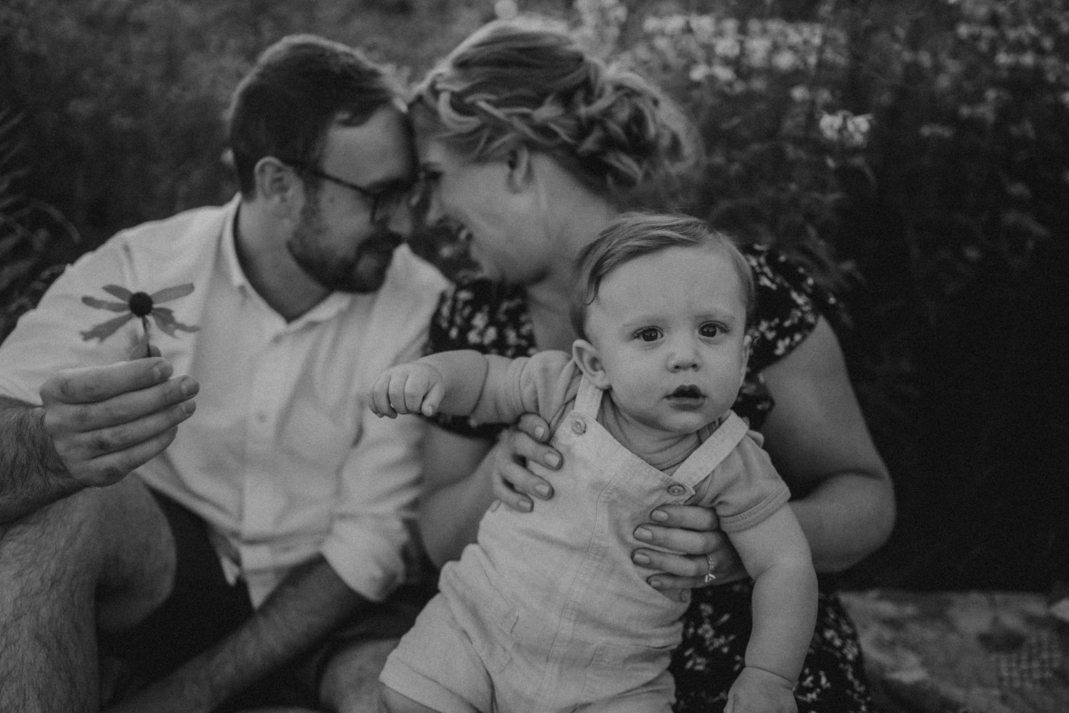 Black and white portrait of family sharing tender moment in wildflower field.