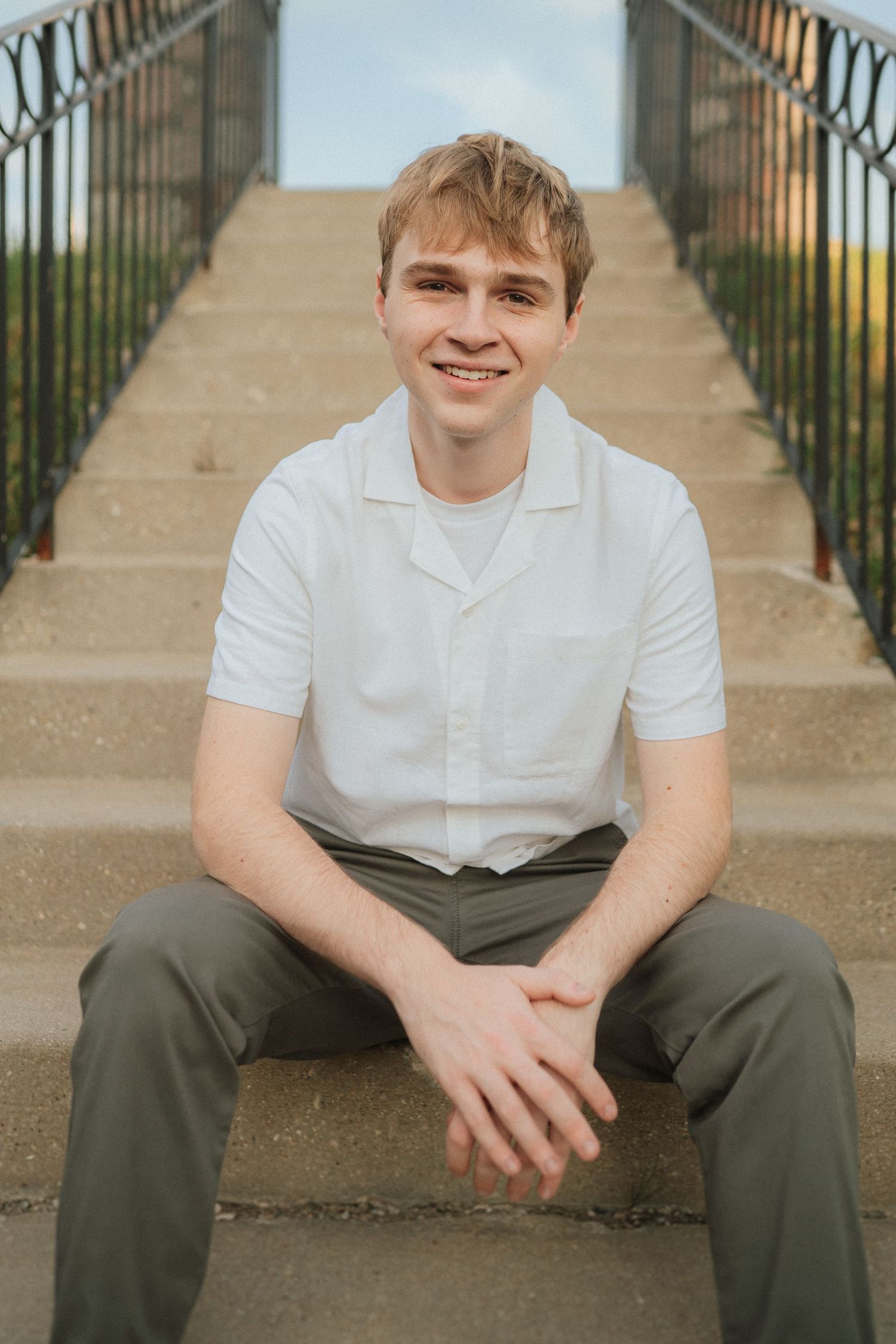 Person in white shirt and olive pants sitting on concrete steps outdoors.