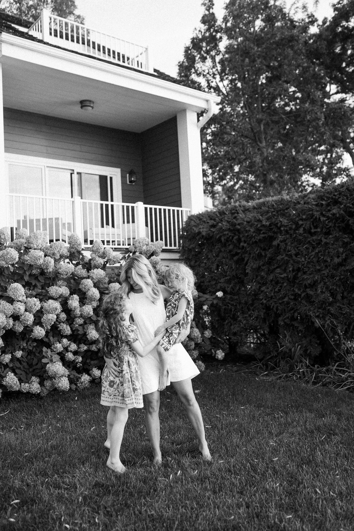Black and white photo of children playing in front of a house with blooming hydrangea bushes.