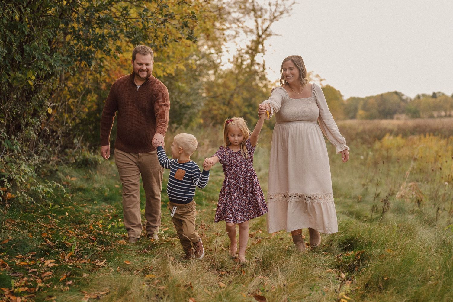 A family walks together through a golden sunlit meadow during sunset, holding hands and sharing joyful moments.
