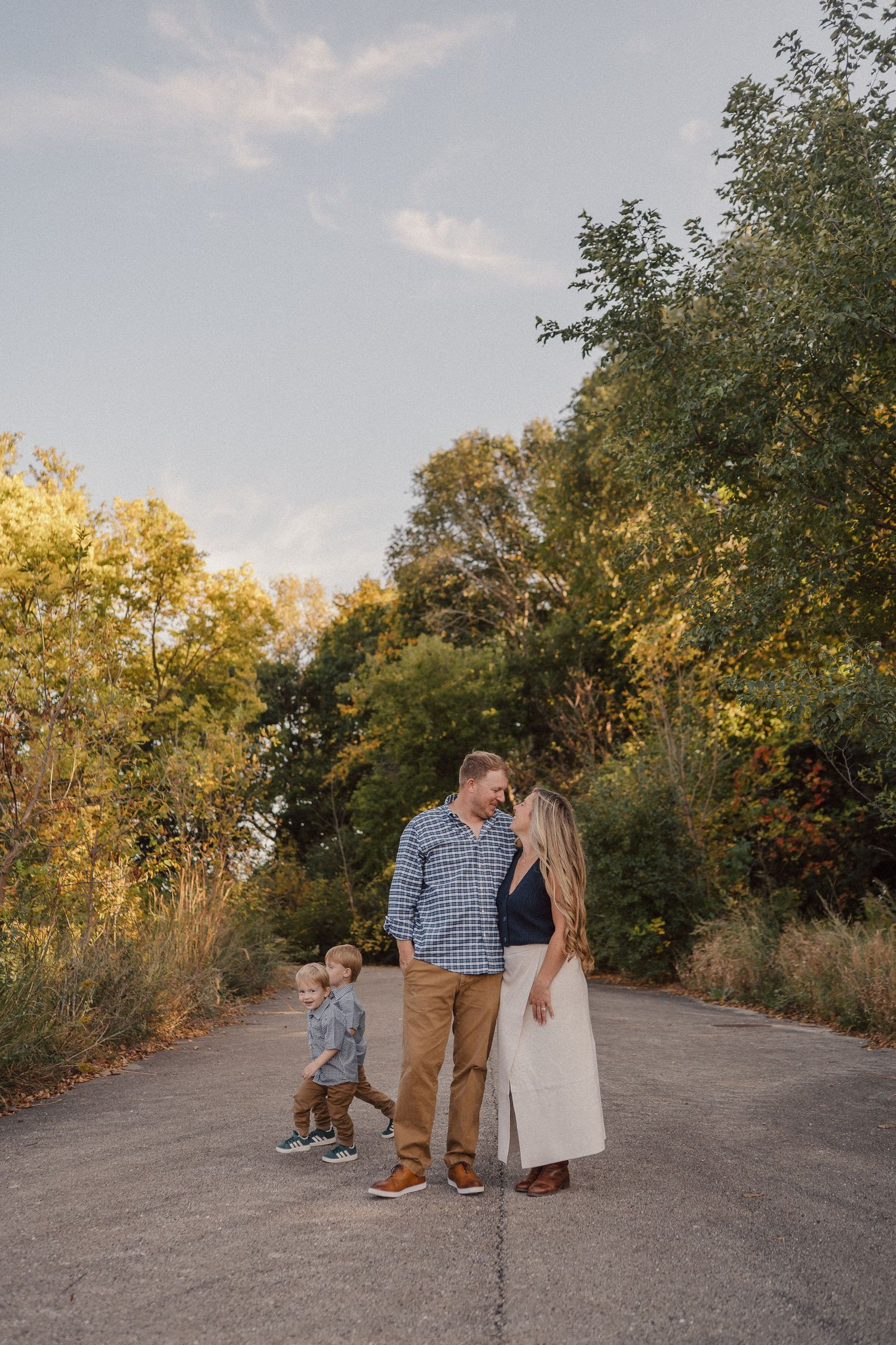 A sweet family portrait session captured on a rustic dirt path surrounded by autumn foliage.