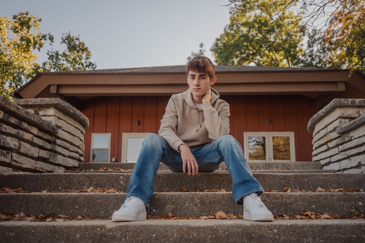 Someone wearing a beige sweater and jeans relaxes on outdoor stone steps during fall.
