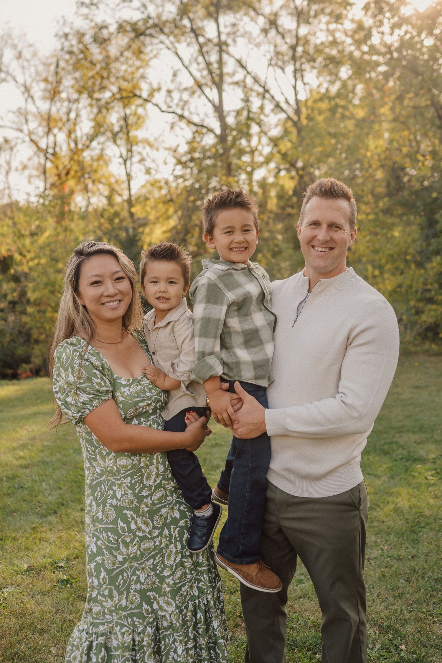A joyful family portrait captured in golden sunlight with autumn trees in the background.