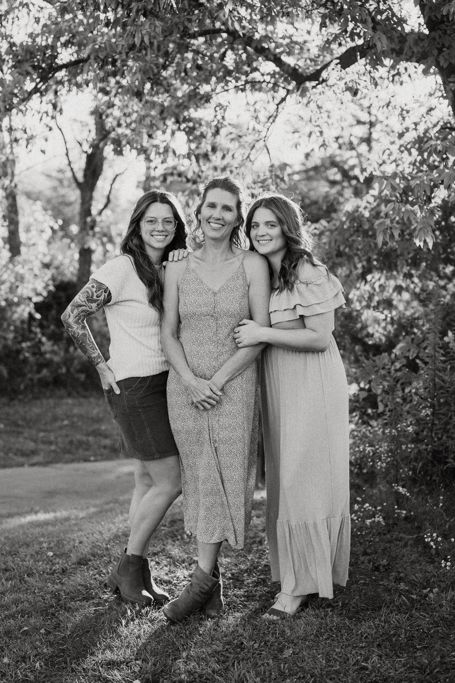Three people embracing outdoors in casual attire against a natural wooded backdrop.