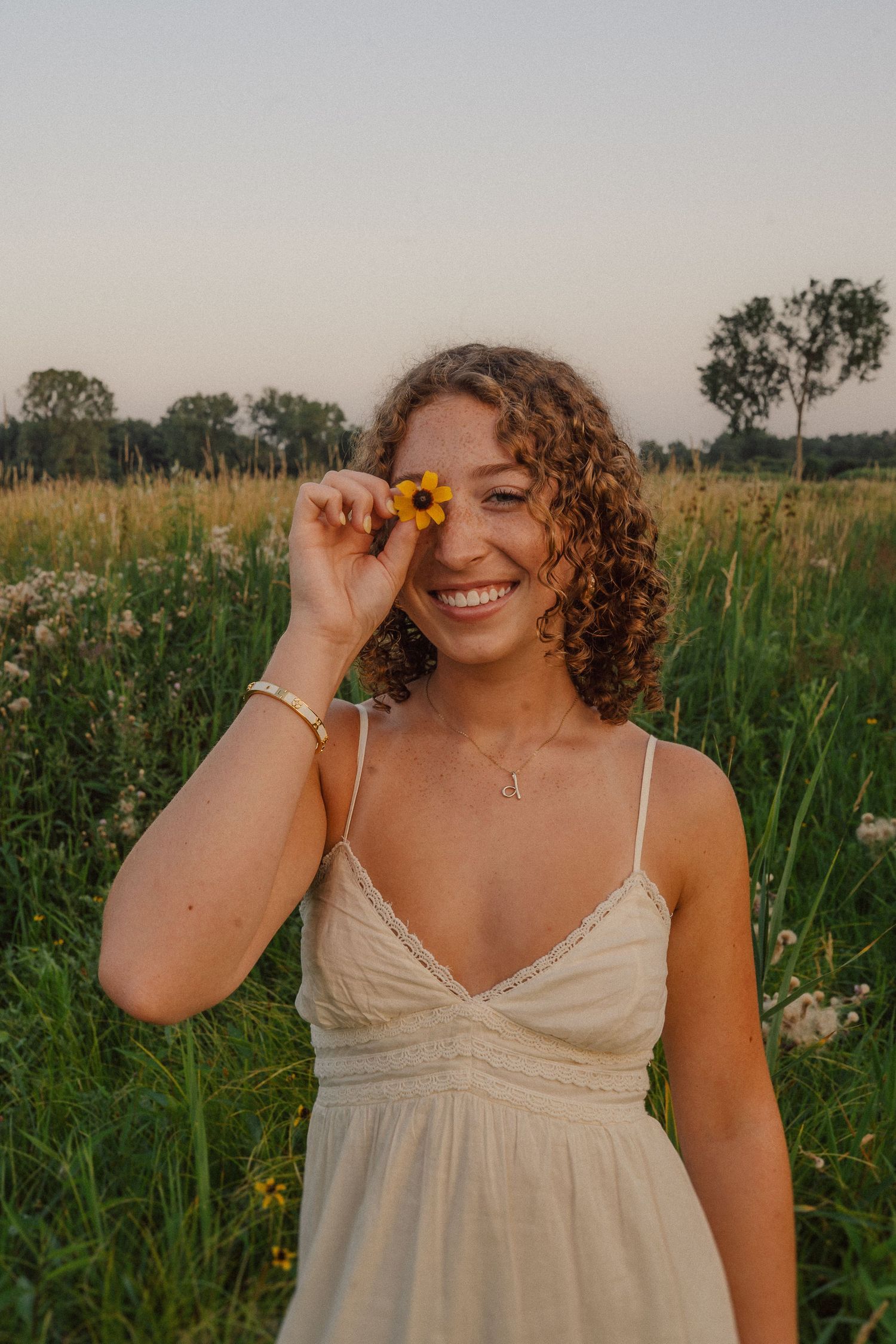 A playful summer portrait in a wildflower field with a yellow flower held to the eye.