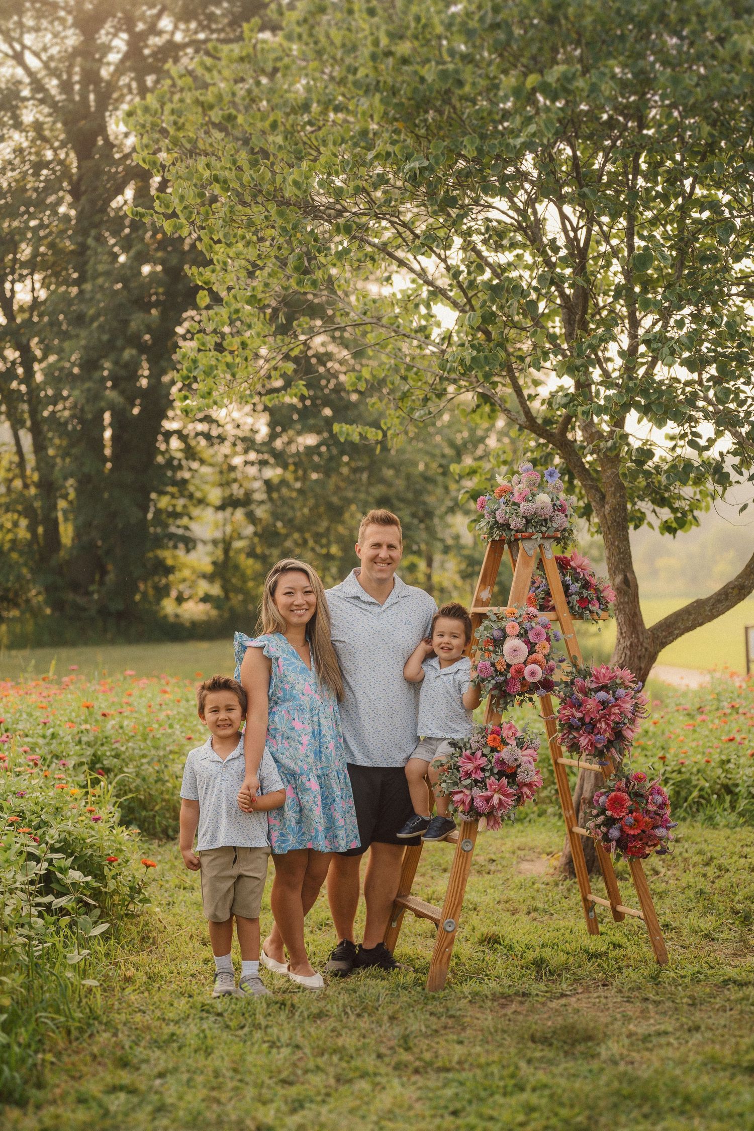 Family in coordinated outfits poses beside wooden swing stand decorated with pink and purple floral arrangements.