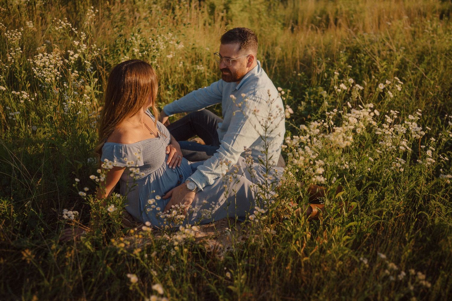 Couple sitting together in a wildflower meadow at golden hour surrounded by white blooming flowers.