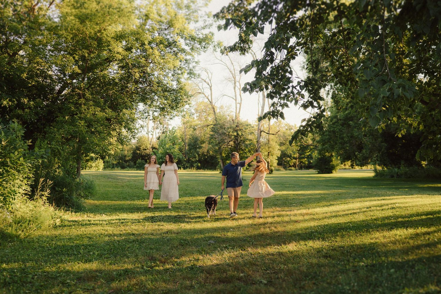 A couple walks through a sunlit park with trees and green grass creating a romantic summer scene.