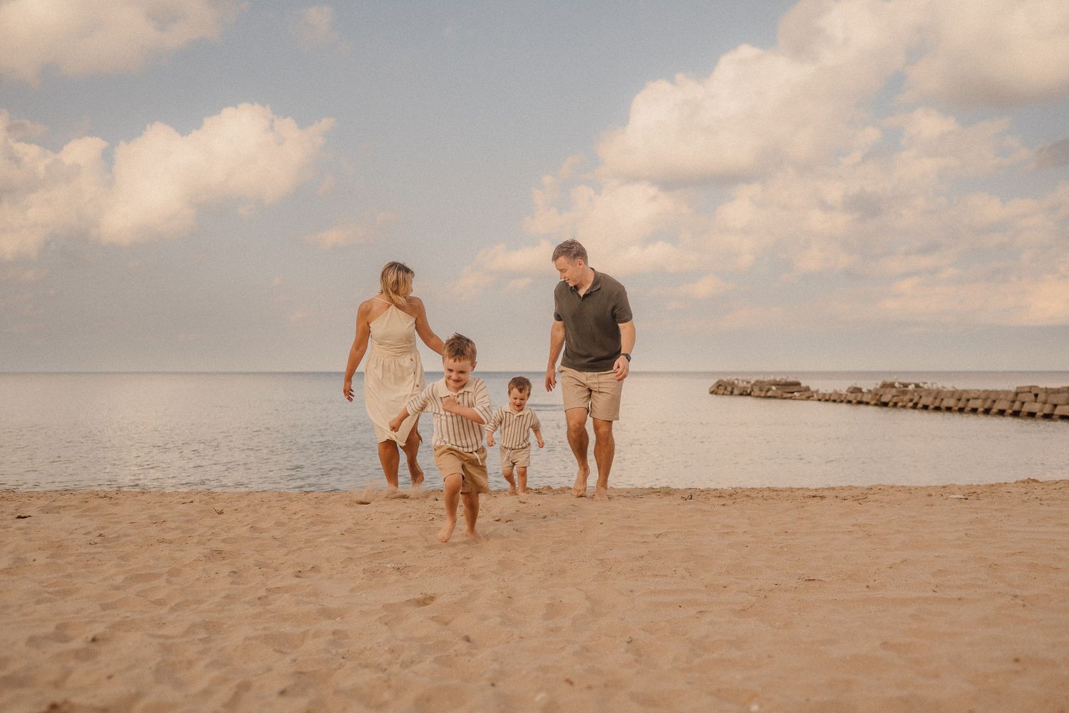 Family walks together on a sandy beach at sunset, enjoying time by the ocean waves and creating silhouettes.