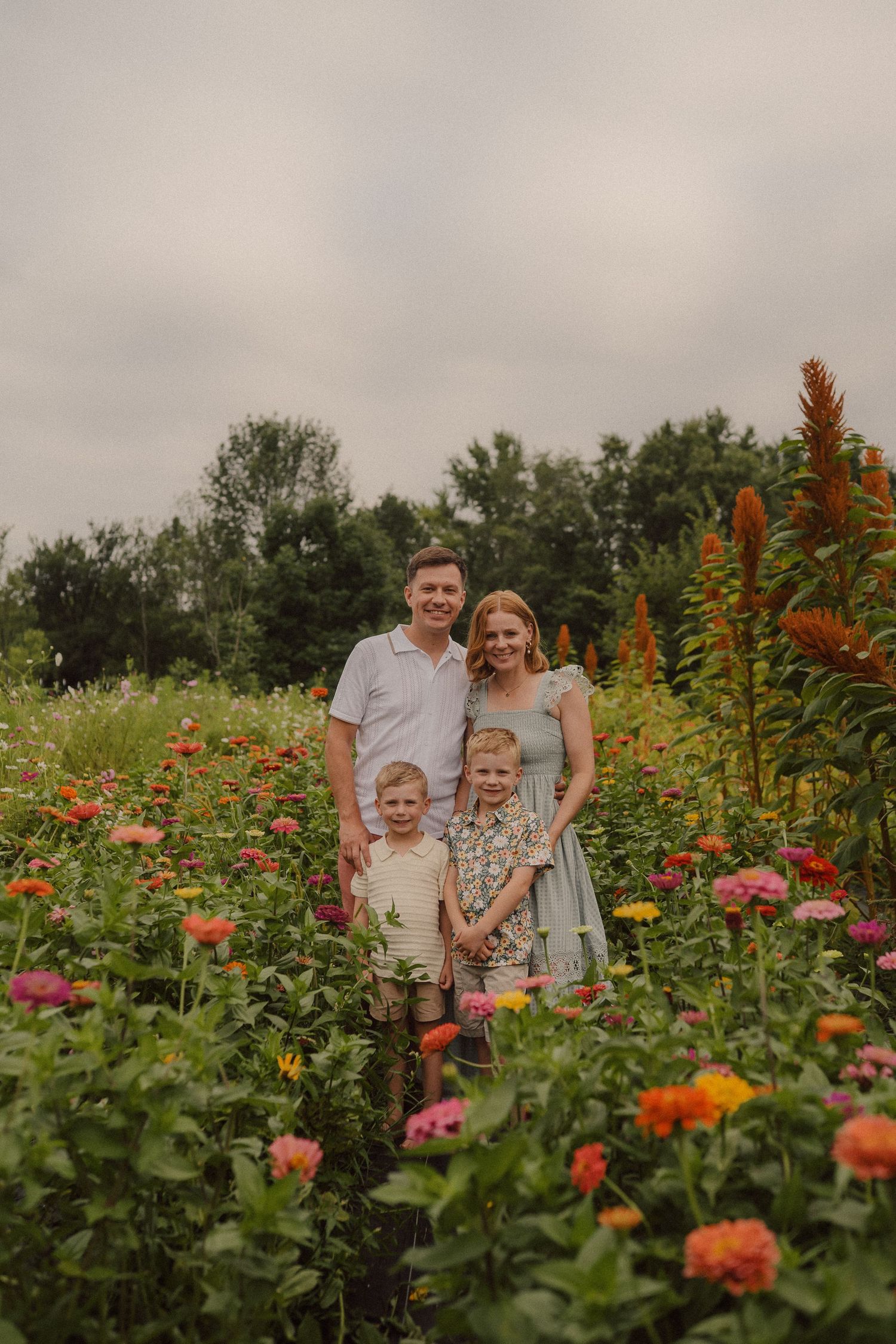 A family enjoys a summer day together in a vibrant flower garden filled with orange and pink blooms.